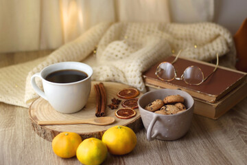 Cup of tea or coffee, various spices, bowl of cookies, tangerines, books, reading glasses and knitted blanket on wooden table. Hygge at home concept, selective focus.