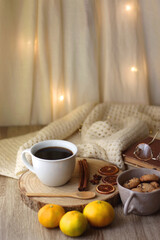Cup of tea or coffee, various spices, bowl of cookies, tangerines, books, reading glasses and knitted blanket on wooden table. Hygge at home concept, selective focus.