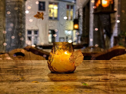  candle on wooden table in city street raing drops on window  falling yellow Autumn leaves in Tallinn old town  seasdon