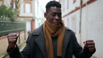 Black man celebrating success clenching fists feeling satisfaction outside in street