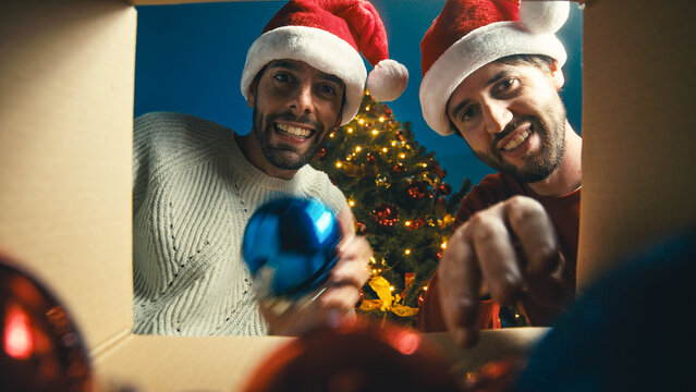 Two boys are taking the balls from the box in Christmas time against the tree
