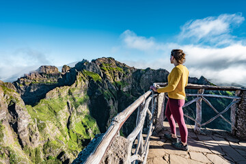 Woman enjoying the mountain scenery of Pico Ruivo from a viewing platform with very steep cliff in...