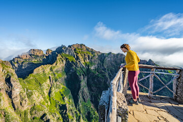 Woman enjoying the mountain scenery of Pico Ruivo from a viewing platform with very steep cliff in the morning. Pico do Arieiro, Madeira Island, Portugal, Europe.