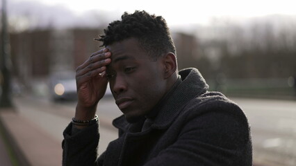 Anxious young black man suffering emotional pain sitting on sidewalk in street