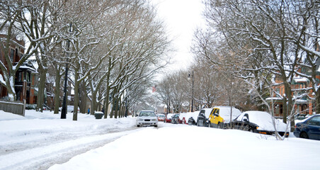 Snow covered street with parked vehicles on the street and incoming vehicle in the winter