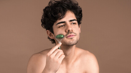 A young caucasian man with stubble beard is doing a facial massage using a roller