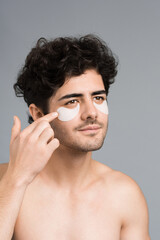 Fototapeta premium A young caucasian man with stubble beard placing patches under his eyes. Vertical view