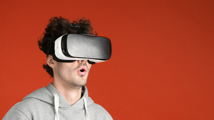 A young man is excited while wearing VR glasses, red background