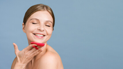 A young caucasian smiling woman is doing a facial massage using face scrubber