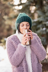Close up portrait of woman walking on winter day, holding travel stainless Steel mug with hot...