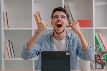 young man or student at desk with laptop celebrating success