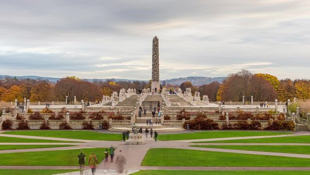 Vigeland (Frogner) park in Oslo Norway in autumn - time lapse of the monolith (monolitten) against clouds in the sky, surrounded by green grass lawn with walking people.