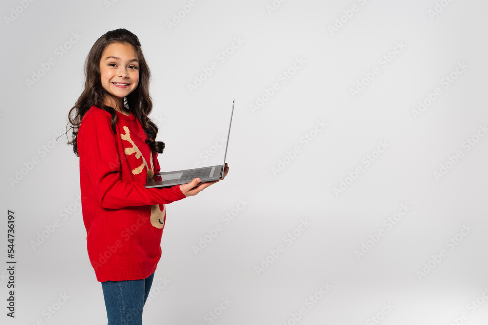 Wall mural happy girl in red Christmas sweater holding laptop isolated on grey