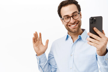 Handsome businessman demonstrating smth on video call. Office worker talking on mobile phone, waving hand, saying hello, white background