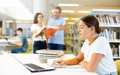 Obraz premium Portrait of young woman studying at library using books and laptop