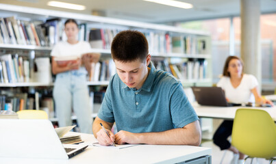 Positive young man in casual clothes working remotely using a computer in a quiet library