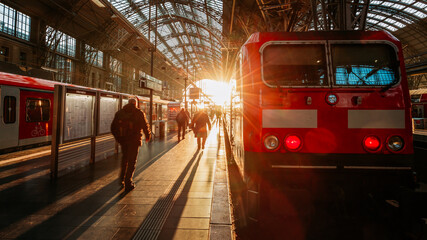 people and train at the train station in direct sunlight in the evening - obrazy, fototapety, plakaty