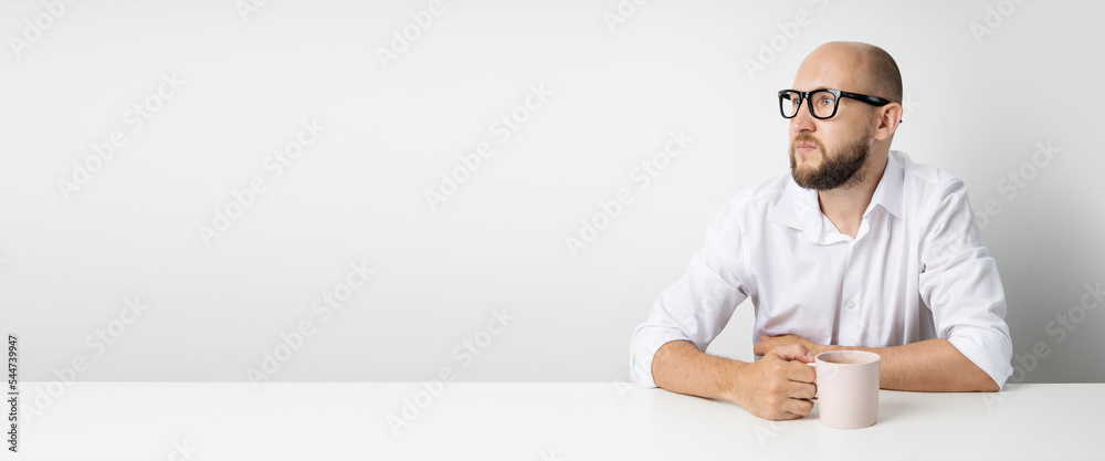 Wall mural pensive young man with a cup sitting at the table on a white background. banner