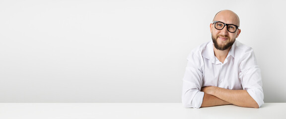 Smiling young man in glasses sitting at the table on a white background. Banner