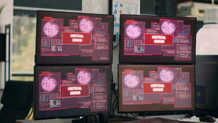 Empty office with multiple monitors showing hacking attack alert, IT agency dealing with security breach warning. Critical error message flashing on screen and computer malfunction.