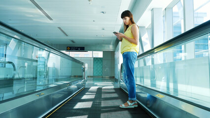 Fototapeta na wymiar Woman standing on Automatic walkway, stairs in subway crossing, using her phone, a mean of communication, a fashionable gadget. The concept is always in touch. High quality photo