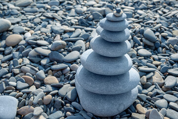 Large tower of stones on Black Sea coast on small pebbles. Tower of stones on seashore is illuminated by sunlight.
