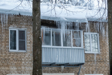 Balcony of small apartment with fogged glass in cold winter. Layer of dangerous and icy icicles hangs from roof to balcony.