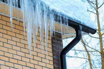 Thick layer of dangerous ice with icicles and snow hanging from roof of house. Ice layer with icicles.