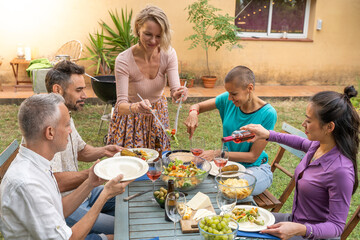 Woman serves the food at house patio. Happy friends laughing around the table outdoor.