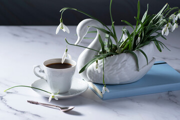 Still life with snowdrops in a ceramic vase like a swan, coffee in a white cup