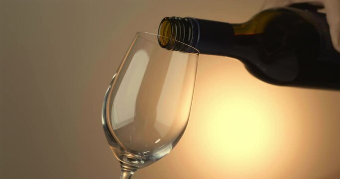 Slow motion of pouring red wine from bottle into goblet on yellow background
