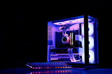 Gaming PC with RGB rainbow LED light. Liquid cooled computer. Powerful PC in a glass case with keyboard. Gamer's workplace in a dark room, neon light.