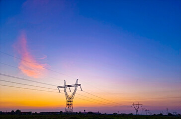 Fototapeta na wymiar High voltage electric poles, rural landscape with power pylons in a row, at sunset