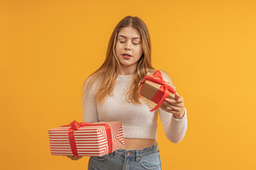 young woman with closed eyes guesses what is in a gift box with a red bow, yellow background