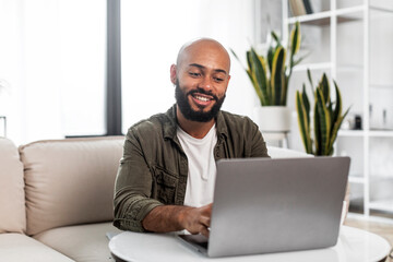 Home office concept. Happy mature man working on pc laptop, sitting on comfy sofa at home and smiling, free space