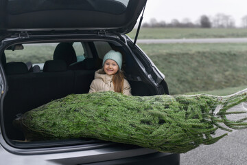 Girl sitting in the trunk with a Christmas tree