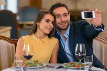 Young couple have romantic dinner in expensive hotel and making selfie photo on phone