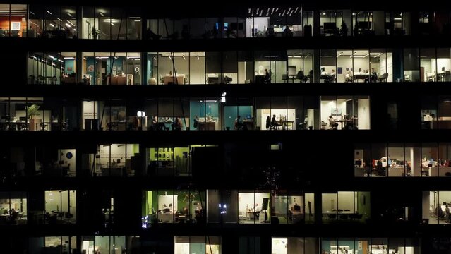 Aerial view office windows lights in modern glass skyscraper at night, illuminated windows texture grid, business center downtown, people working in open space in evening, end of working day