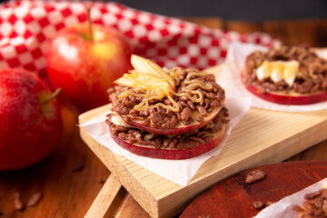 Creative party snack for holidays. Apple rounds with peanut butter, caramel and chocolate flavor puffed rice topping with banana slices. Funny appetizer for kids and adults.