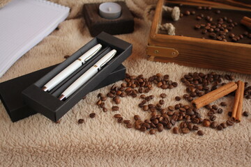 The pen is on the table. Coffee, a wooden tray of cinnamon, and a candle are strewn nearby. Morning. Postcard for the inscription of wishes.