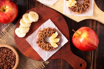 Creative party snack for holidays. Apple rounds with peanut butter, caramel and chocolate flavor puffed rice topping with banana slices. Funny appetizer for kids and adults.