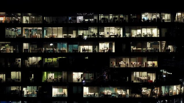 Aerial view office windows lights in modern glass skyscraper at night, illuminated windows texture grid, business center downtown, people working in open space in evening, end of working day