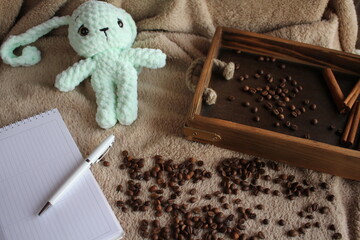 Fototapeta premium A soft toy lies on a table on a plush blanket. There is a wish card next to it. Coffee beans and a wooden tray complete the decor. Handmade. Hobby. Knitting. Gifts for the holidays.