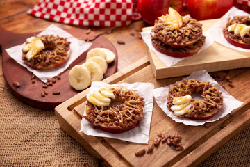 Fototapeta na wymiar Creative party snack for holidays. Apple rounds with peanut butter, caramel and chocolate flavor puffed rice topping with banana slices. Funny appetizer for kids and adults.