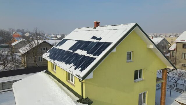 Aerial view of snow melting from covered solar photovoltaic panels installed on house rooftop for producing clean electrical energy. Low effectivity of renewable electricity in nothern region winter
