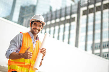 Young caucasian man holding a big paper, a guy wearing a light blue shirt and jeans with an orange vest and white helmet for security in a construction area.