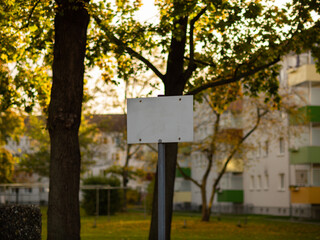 Blank sign in a backyard area. Weathered dirty white plate with many dirt spots. Template for information messages in a residential district. Autumn trees are in the background.