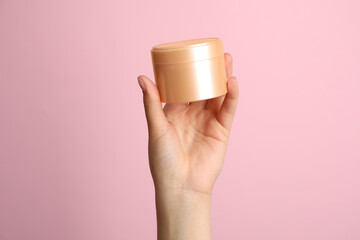 Woman holding jar of face cream on pink background, closeup
