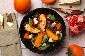 Delicious persimmon salad, knife and fork on tiled surface
