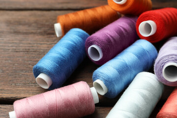 Different colorful sewing threads on wooden table, closeup